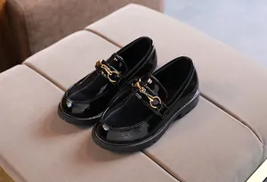 Macro shot of black patent leather kids loafers with vintage gold horsebit buckle detail
