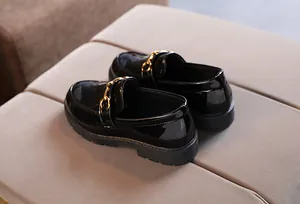 Detailed close-up of shiny black patent leather kids loafers with gold horsebit buckle