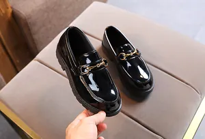 Close-up of children's black patent leather loafers featuring a golden horsebit detail