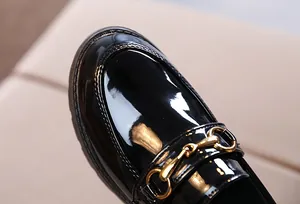Macro detail of glossy black patent leather shoe with iconic golden horsebit buckle