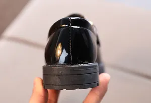 Detailed close-up of glossy black patent leather child shoes with non-slip rubber soles