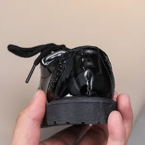 Gros plan de chaussures richelieu en cuir verni noir pour enfants avec détails perforés