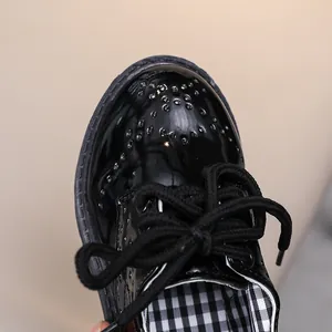 Détail de chaussures en cuir verni noir pour enfants avec broderies et doublure écossaise