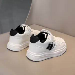 Detail of white leather kids sneakers with bear embroidery and velcro strap on a chair