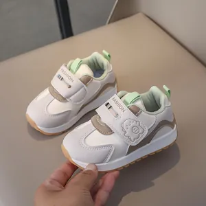 Detail view of toddler white sneakers featuring dual velcro straps and cartoon monster pattern