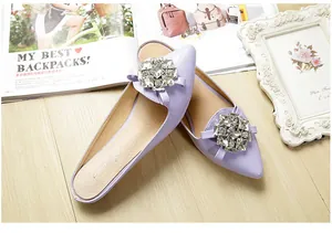 Detail of light purple pointed-toe mule shoes with crystal buckle on wood floor