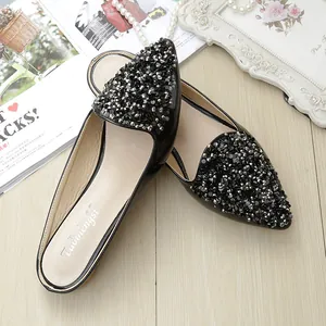 Elegantes mules negros de punta con lentejuelas brillantes sobre suelo de madera