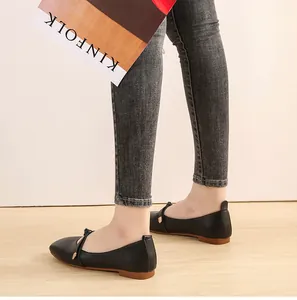 Detail of black square-toe flats with thin buckle strap and brown sole worn on model