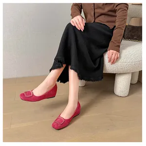 Detail of red suede ballet flats with a square buckle on a cozy white chair