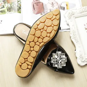 Detail view of black patent leather flats with rhinestone buckle and fruit-patterned rubber sole