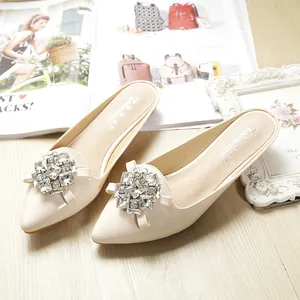 Detailed view of beige pointed-toe mules with large geometric rhinestone embellishments