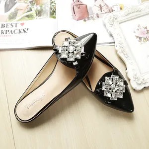 Macro detail of glossy black patent leather pointed mule with sparkling rhinestone buckle