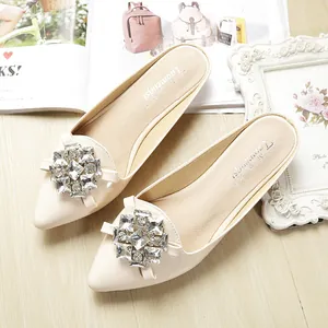 Elegant beige pointed-toe flat mules with rhinestone buckle on a stylish wooden floor