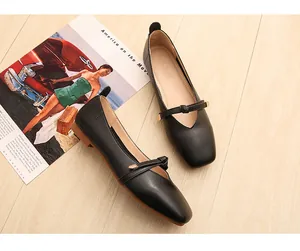 Scarpe Mary Jane piatte in pelle nera con cinturino a fiocco su fondo legno
