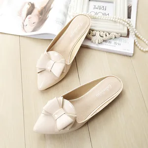 Elegant beige pointed-toe flat mules with a bow accent on a wooden surface