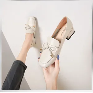 Détail de mocassins crème à bout carré avec un nœud doré et un talon épais noir élégant