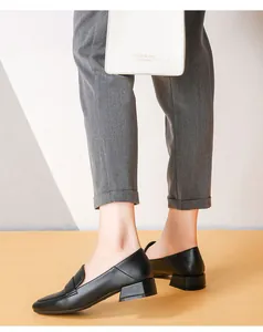 Primer plano de mocasines negros de punta cuadrada con tacón grueso y pantalones grises