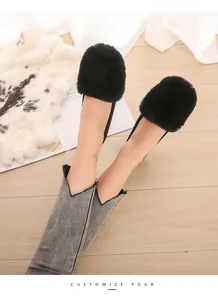 Detailed view of women's black flat fur loafers with rabbit fur on a light wood floor