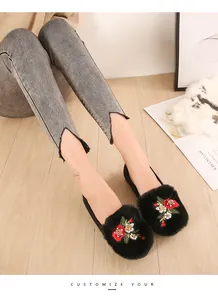 Détail de ballerines noires en fourrure avec broderie florale et jean gris effiloché