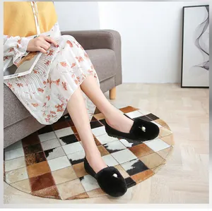 Detalle de mocasines negros de felpa con perla sobre alfombra suave de interior