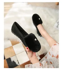 Detalle de mocasines negros de ante con pompón de pelo y perla sobre alfombra