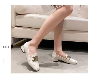 Detail of off-white loafers with gold buckle and chunky heel shown on feet