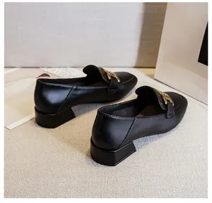 Close-up of black matte loafers with gold metal H-buckle on textured beige fabric