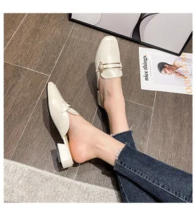 Primer plano de mules blanco crema con dije de perla saturno en suelo de madera oscura