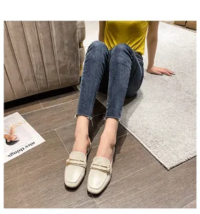 Detalle de mule blanco crema con barra dorada y perla sobre una revista de moda
