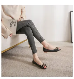 Detail of black peep-toe flat shoes with gold chain buckle worn with grey jeans