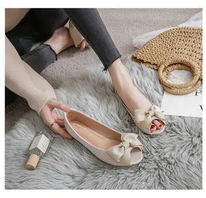 Nahaufnahme cremefarbener Peep-Toe Ballerinas mit Satinschleife auf grauem Teppich