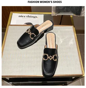 Detail view of black square-toe mule with rhinestone horsebit buckle on a white surface