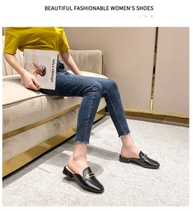 Detalle de mules negros con hebillas doradas y perlas usados con jeans en la alfombra