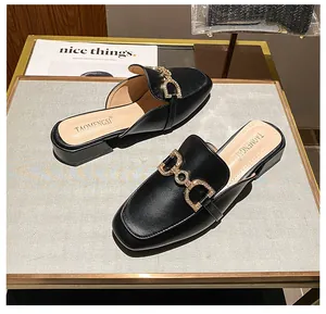 Top view of black pointed toe mules with gold rhinestone buckle on leather surface