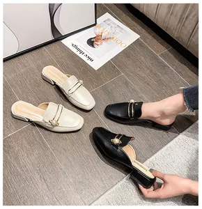 Detalle de mules con perlas y barra dorada sobre acabado de cuero sintético mate elegante