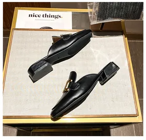 Detailansicht schwarzer Leder-Mules mit eleganter goldener Metallschnalle und Blockabsatz