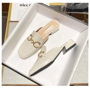 Detailed close-up of cream-colored mule shoes with rhinestone gold chain buckle and block heel