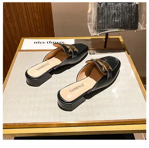Detail eines schwarzen Leder-Mules mit polierter Goldkettenschnalle auf einem Displayständer
