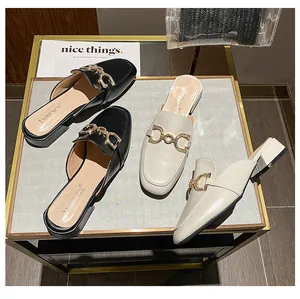 Close-up of square-toe mule sandals featuring golden metal chains and rhinestone accents