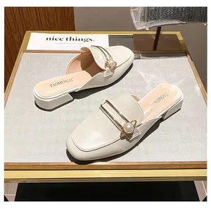 Detalle de mules beige con barra metálica dorada y hebilla de perla en zapato plano