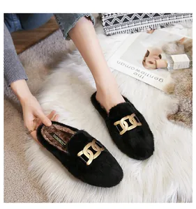 Close-up of black fuzzy flat mules featuring a decorative gold chain on soft plush rug