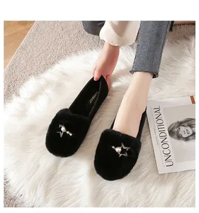 Detail van zwarte faux fur loafers met ster-parel gesp op een wit pluche tapijt