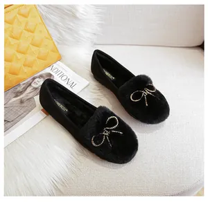 Detailed view of black faux fur flat shoes featuring a delicate gold beaded bow ornament