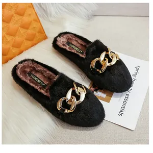 Detail view of black plush flat mule with stylish gold chain buckle on a soft white rug