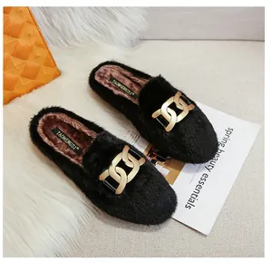 Detail of black faux fur flat mules featuring a gold chain buckle and plush brown lining