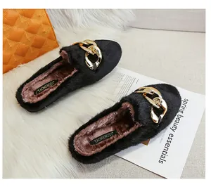 Close-up of black faux fur mule slippers with a bold gold chain link buckle detail