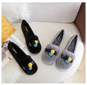 Vista piatta di mocassini in peluche con fiocco decorativo e dettagli di pompon colorati