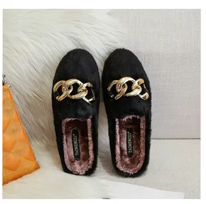 Detail of black faux fur mule slippers featuring a large gold chain buckle and plush lining