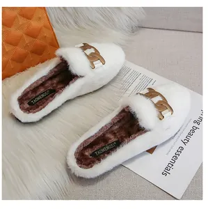 Detailed close-up of white plush mule slipper featuring golden chain and soft brown lining