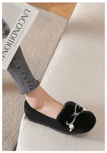 Close-up of black plush slip-on shoes with rhinestone bow and pearl fur ball decor
